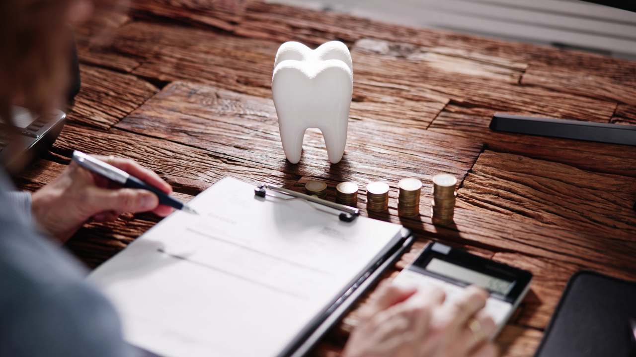 Tooth model and coins on desk illustrating dental malpractice insurance cost