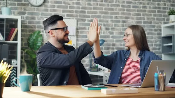a man and a woman sitting at a desk in an office sharing a high five