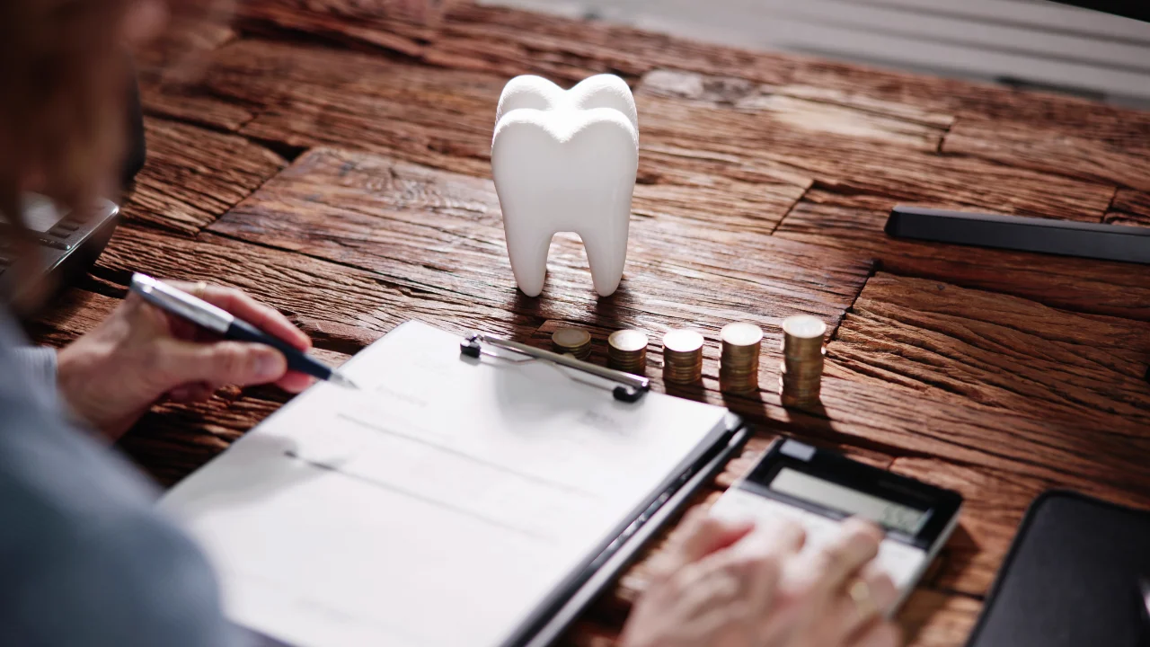 Tooth model and coins on desk illustrating dental malpractice insurance cost